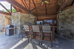 An outdoor kitchen area with stone walls, a grill, and bar stools. - Golf View 2 Bedroom Cabin by RedAwning (Pigeon Forge)