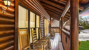 A wooden log cabin with a covered porch and several wooden chairs. - Golf View 2 Bedroom Cabin by RedAwning (Pigeon Forge)