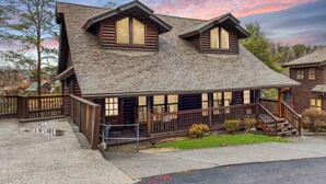 A log cabin with a porch, two large windows, and a staircase leading to the entrance. - Golf View 2 Bedroom Cabin by RedAwning (Pigeon Forge)