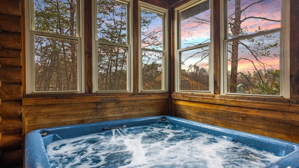 A wooden cabin with a hot tub and large windows overlooking a forest. - Golf View 2 Bedroom Cabin by RedAwning (Pigeon Forge)