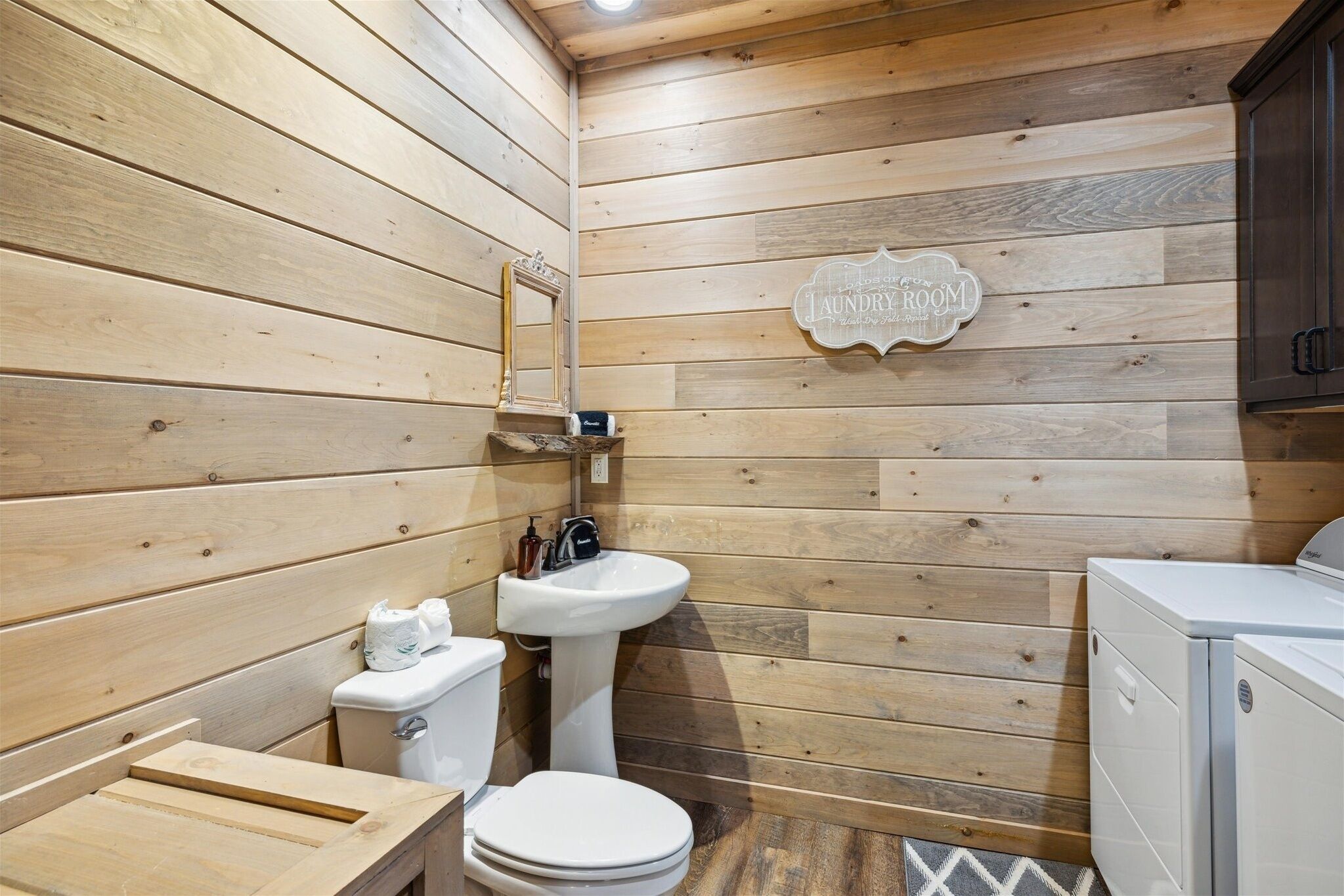A compact wooden bathroom with a toilet, sink, and washing machine.
