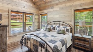 A bedroom with a bed, a nightstand, a ceiling fan, and large windows with blinds. - Antler Ridge 3 Bedroom Cabin by RedAwning (Sevierville)