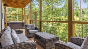 A covered outdoor deck with wicker furniture, a hot tub, and a view of a forest. - Antler Ridge 3 Bedroom Cabin by RedAwning (Sevierville)