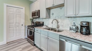 A kitchen with white cabinets, a microwave, a stove, a sink, and a coffee maker.