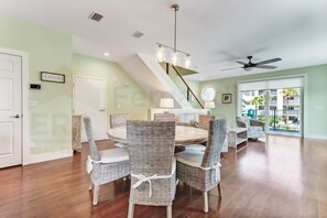 A spacious living area with a dining table, wicker chairs, a staircase, and a large window offering a view of the outdoors. - 391 A&b 4 Bedroom Townhouse by RedAwning (Fernandina Beach)