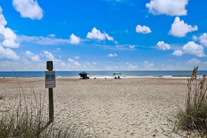 Ein Strand mit einem Wegweiser, zwei Strandsonnenschirmen und dem Meer im Hintergrund.