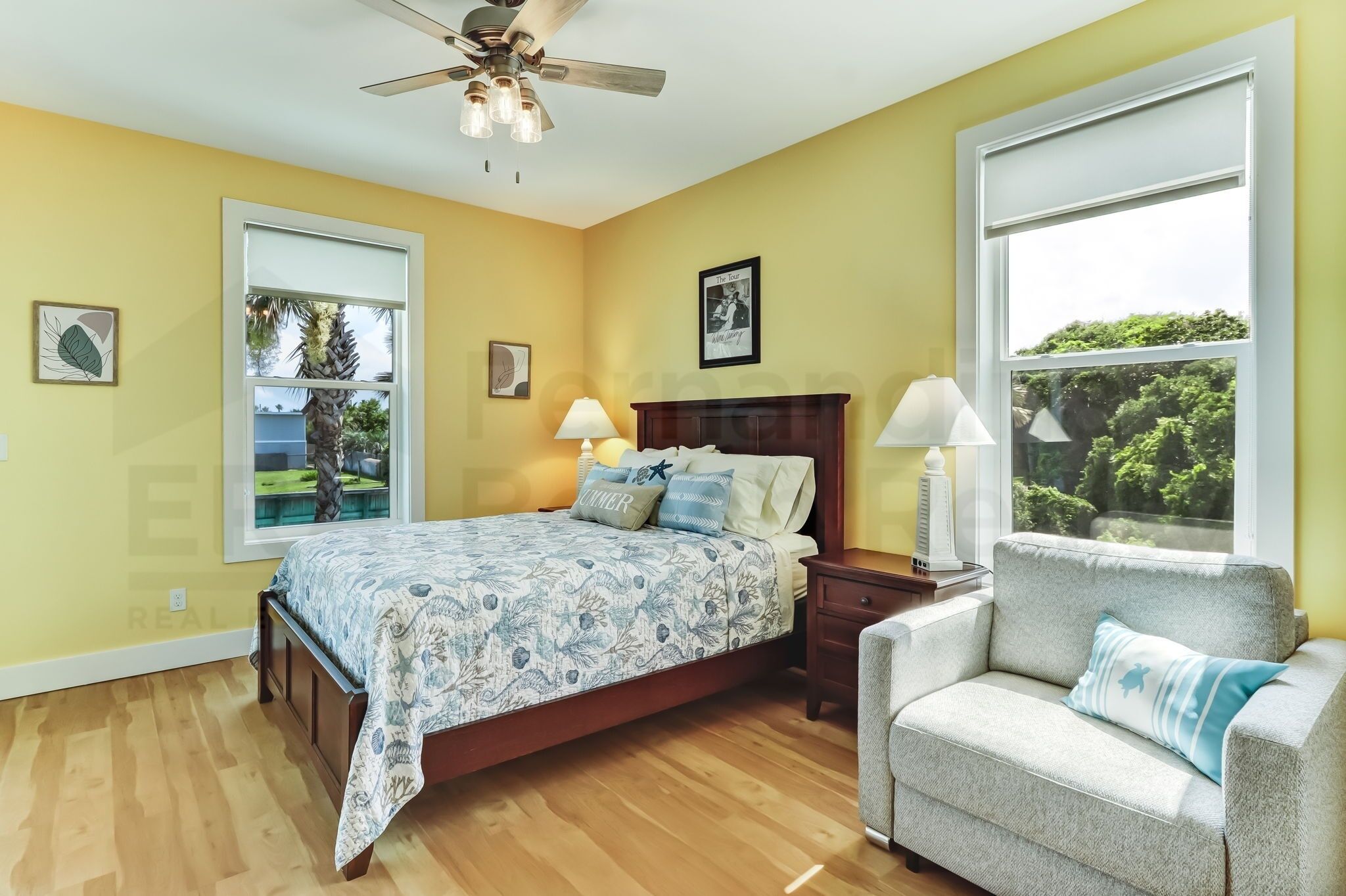 A bedroom with a bed, bedside tables, a chair, a ceiling fan, and large windows.