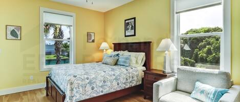 A bedroom with a bed, bedside tables, a chair, a ceiling fan, and large windows.