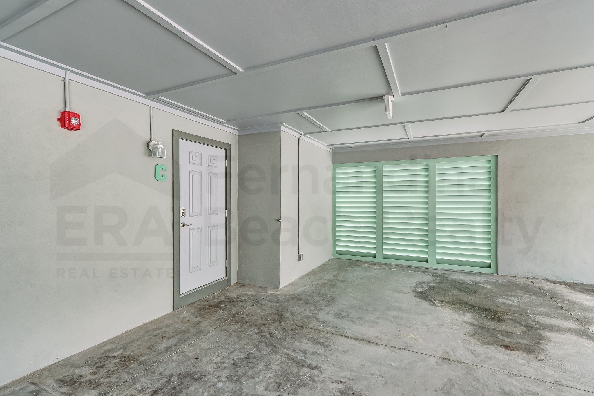 A clean, empty room with a concrete floor, a white door, and green shutters on the window.
