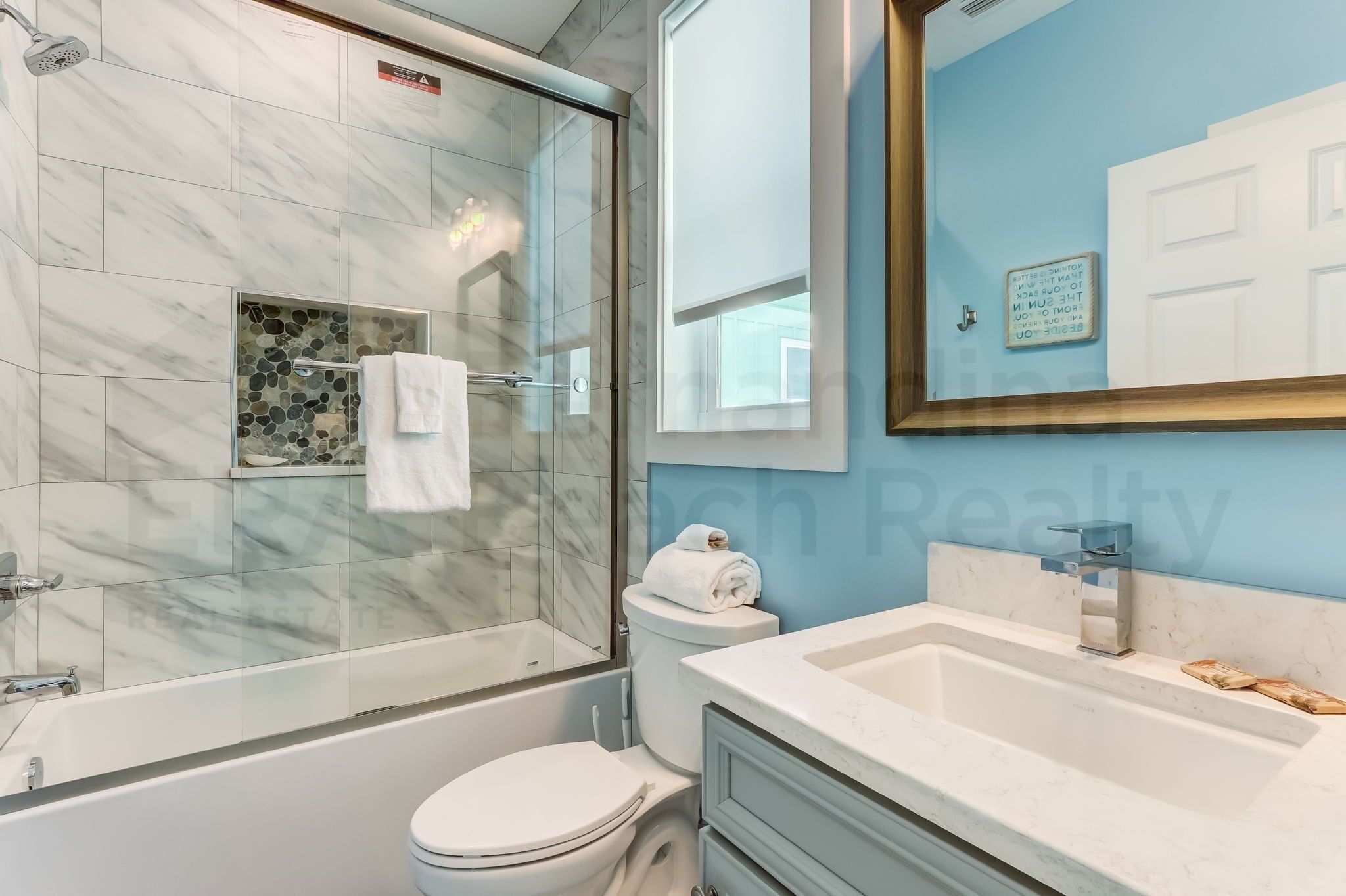 A modern bathroom with a glass-enclosed shower, a white toilet, and a sink with a marble countertop.