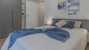 A neatly made bed with a blue blanket, a bedside lamp, and two abstract paintings on the wall. - La casa del Sarto_varennaholidays (Perledo)