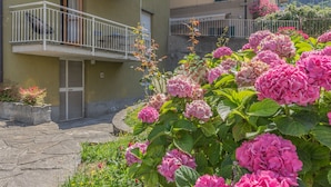 A residential building with balconies, a stone pathway, and pink hydrangea bushes. - La casa del Sarto_varennaholidays (Perledo)