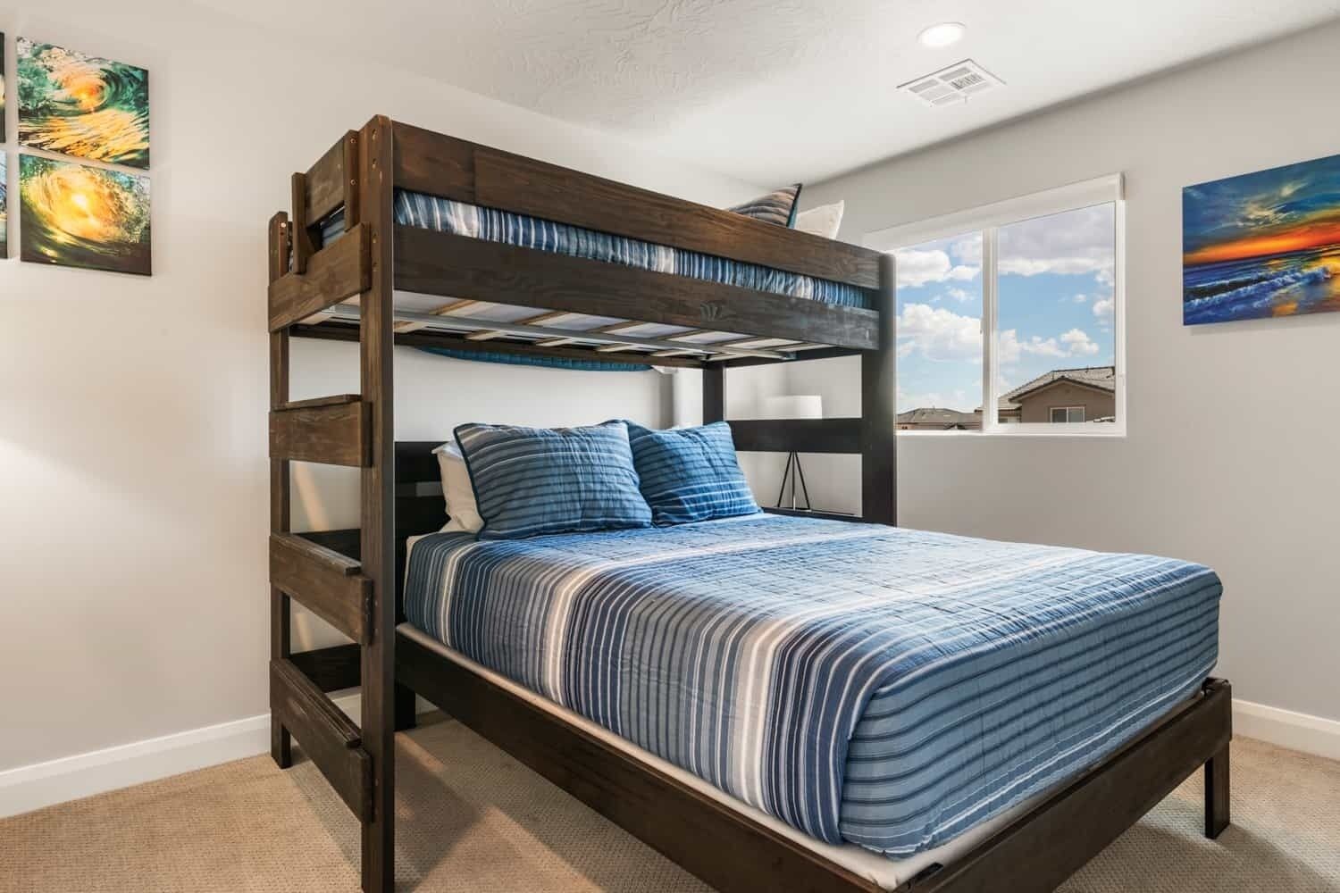 Un lit superposé avec une couette à rayures bleues et blanches, une structure en bois et une fenêtre donnant sur une maison.