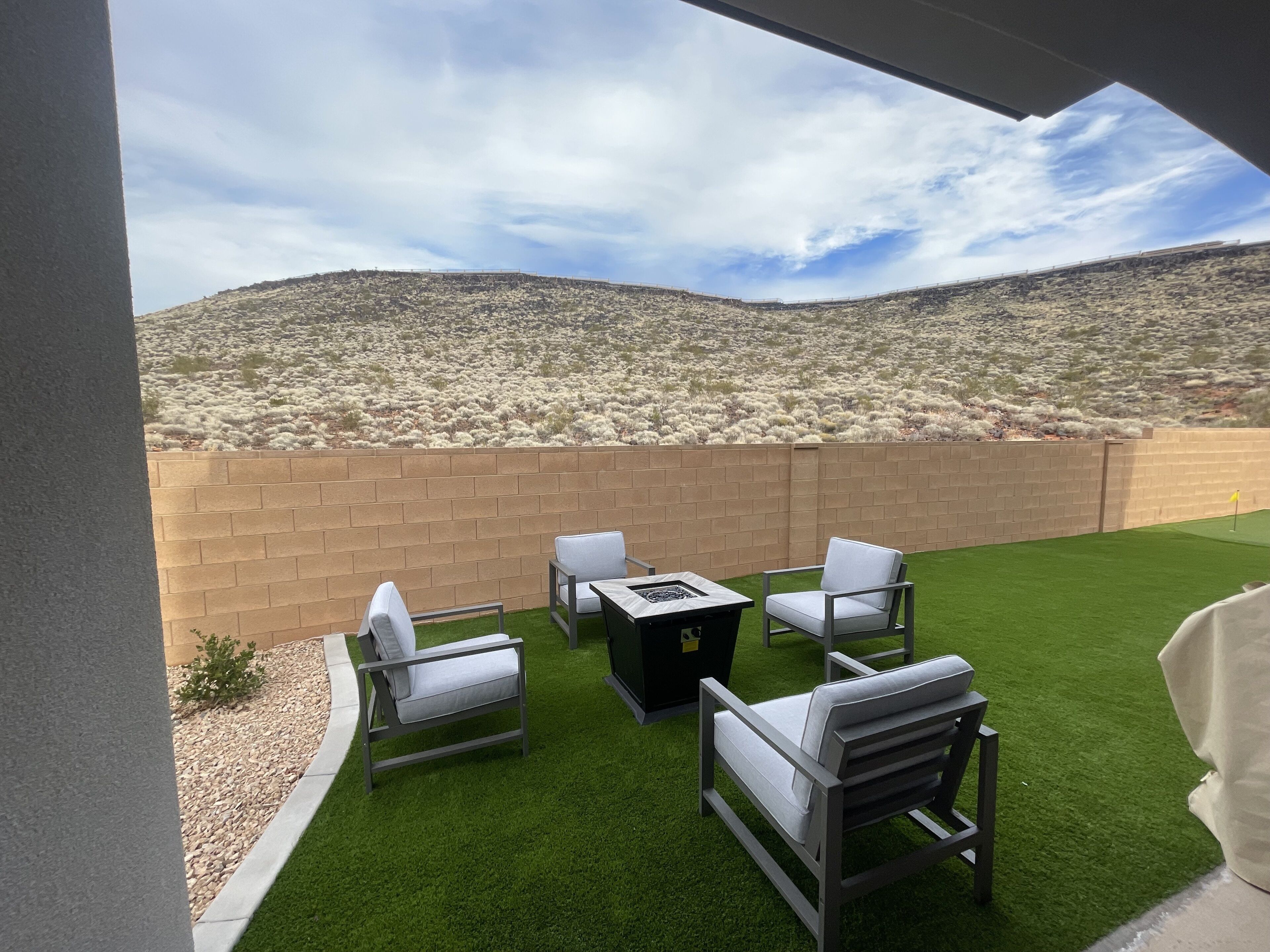 An outdoor patio with a brick wall, artificial grass, and outdoor furniture.