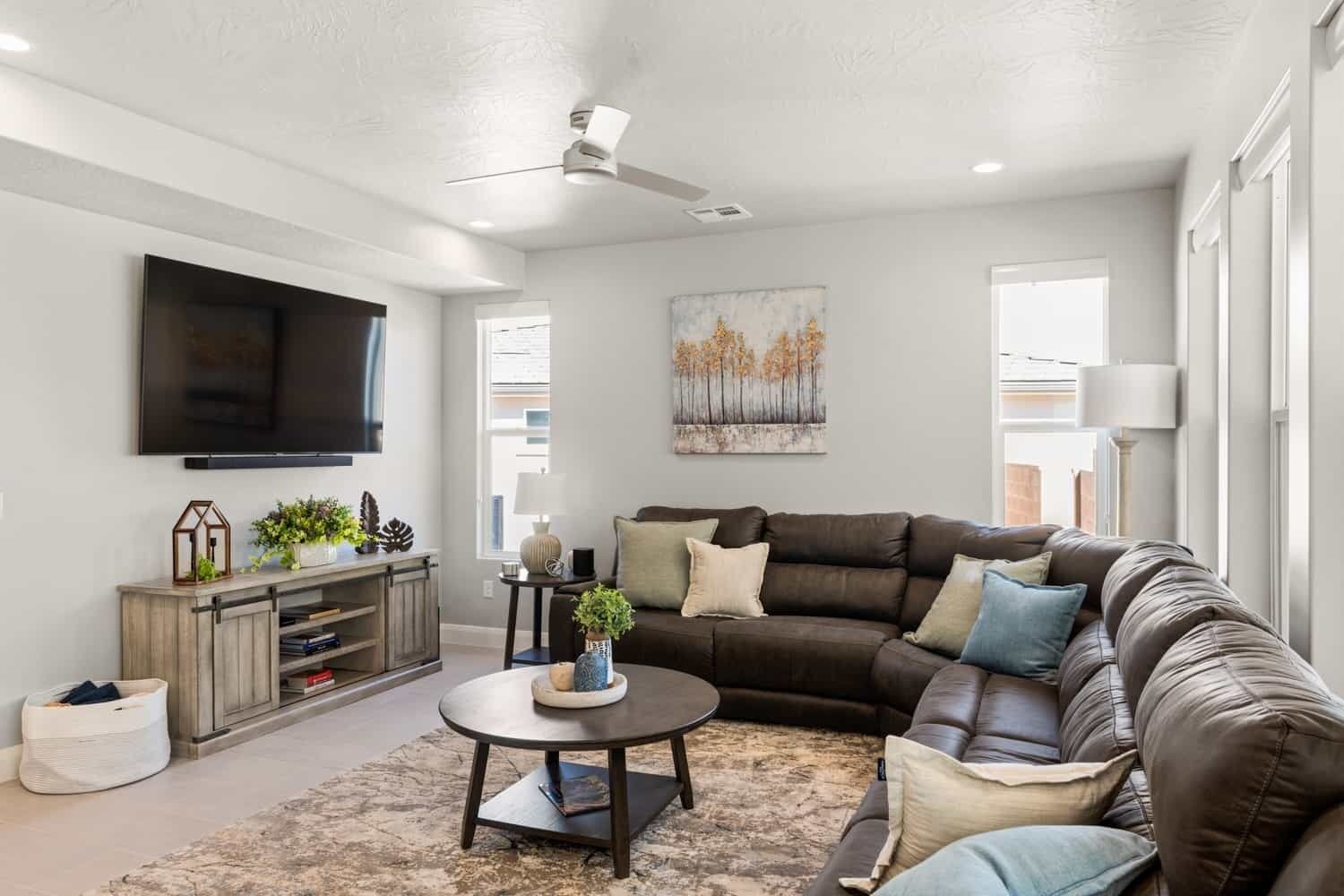 A modern living room with a sectional sofa, a flat-screen TV, a ceiling fan, and a painting on the wall.