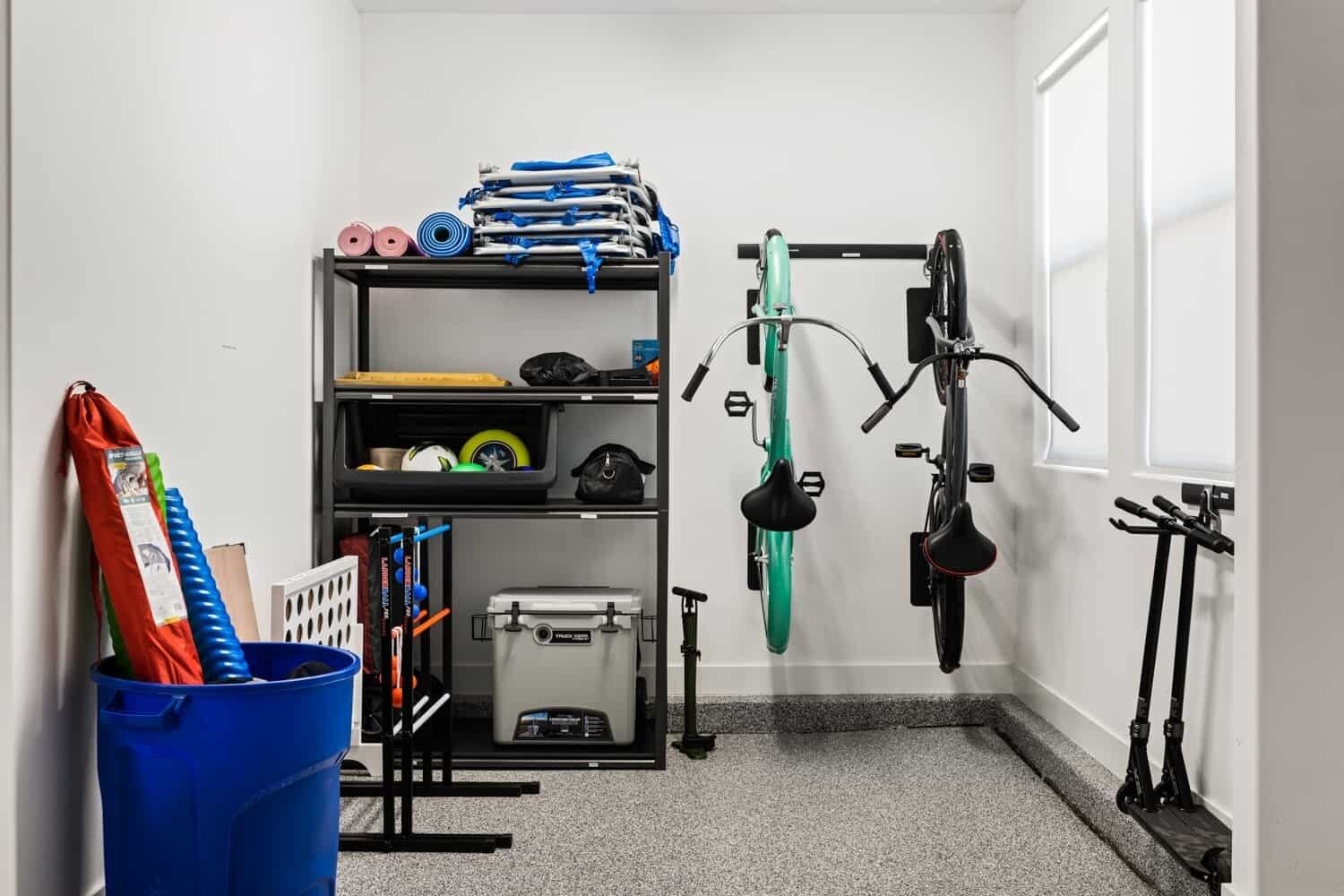 Habitación compacta con un estante en la pared que contiene equipo de ejercicio, un cubo de basura azul y un pequeño armario.