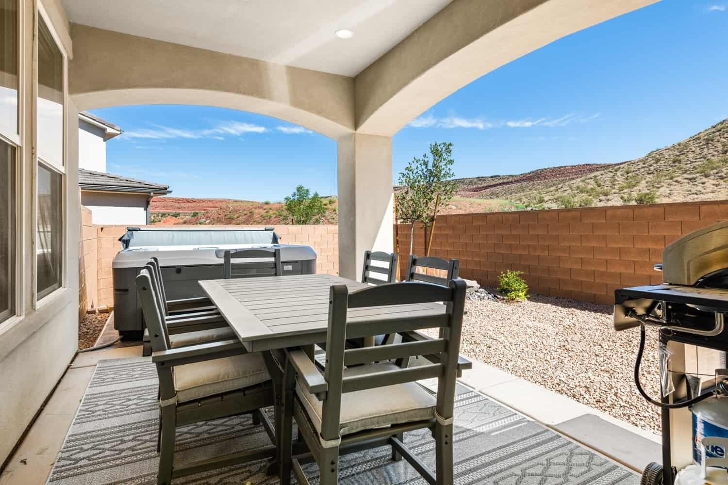 An outdoor patio with a table and chairs, a barbecue grill, and a view of a desert landscape.