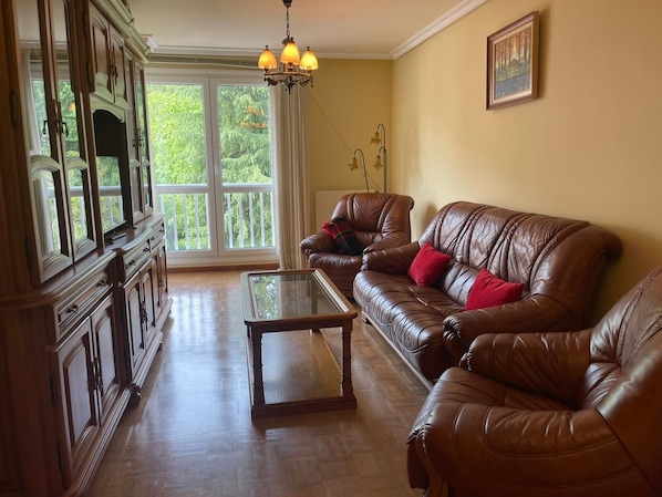 A living room with a brown leather sofa, a glass coffee table, and a wooden cabinet.