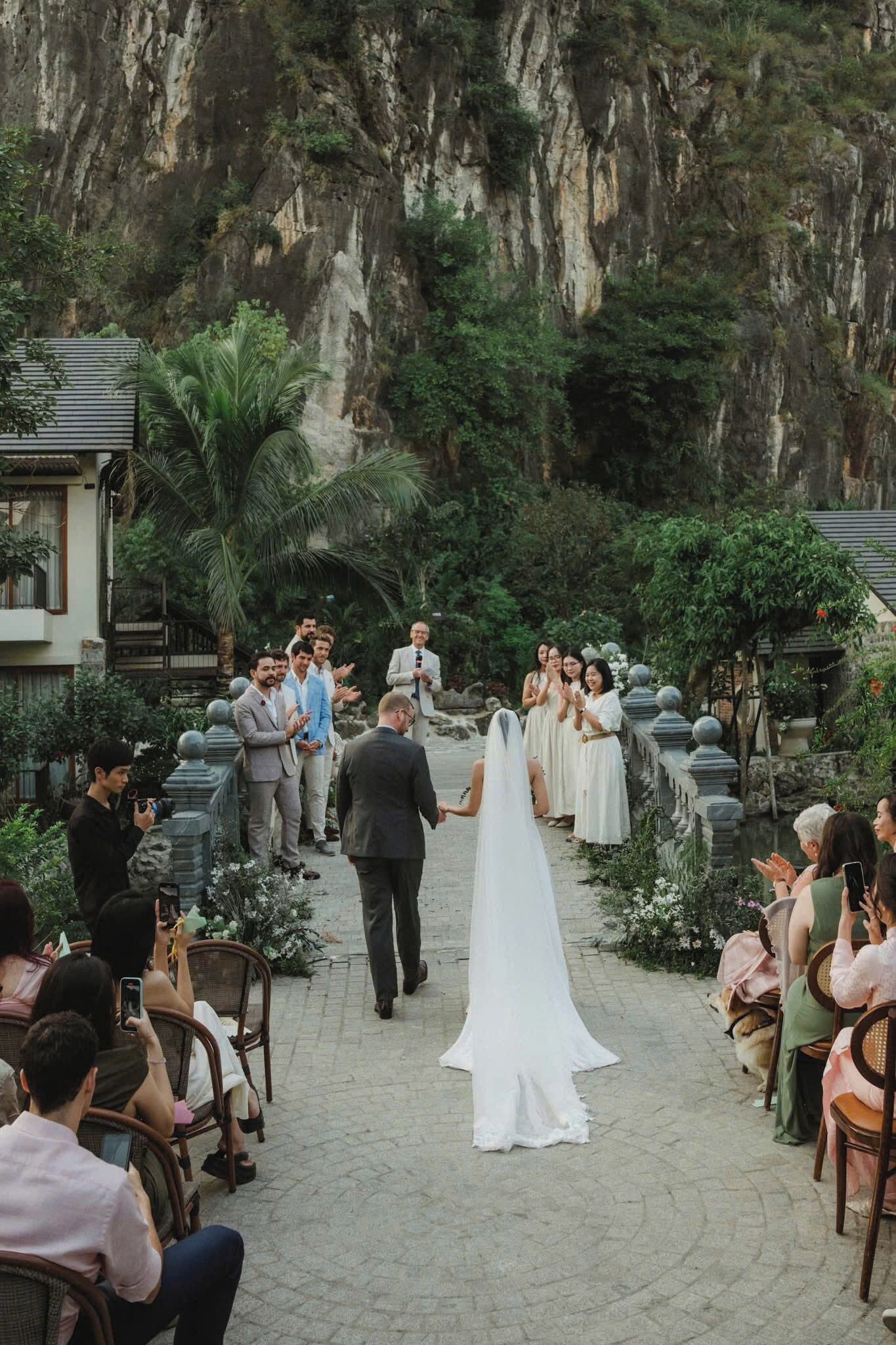 A wedding ceremony in a garden with stone walls and tropical plants.