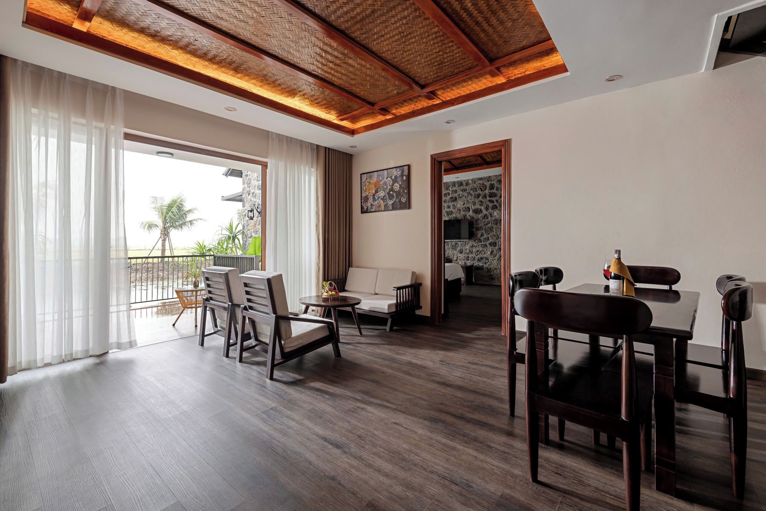 A spacious living area with a wooden ceiling, a dining table with chairs, a sofa, and a view of the outdoors.