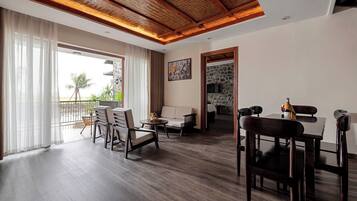 A spacious living area with a wooden ceiling, a dining table with chairs, a sofa, and a view of the outdoors.