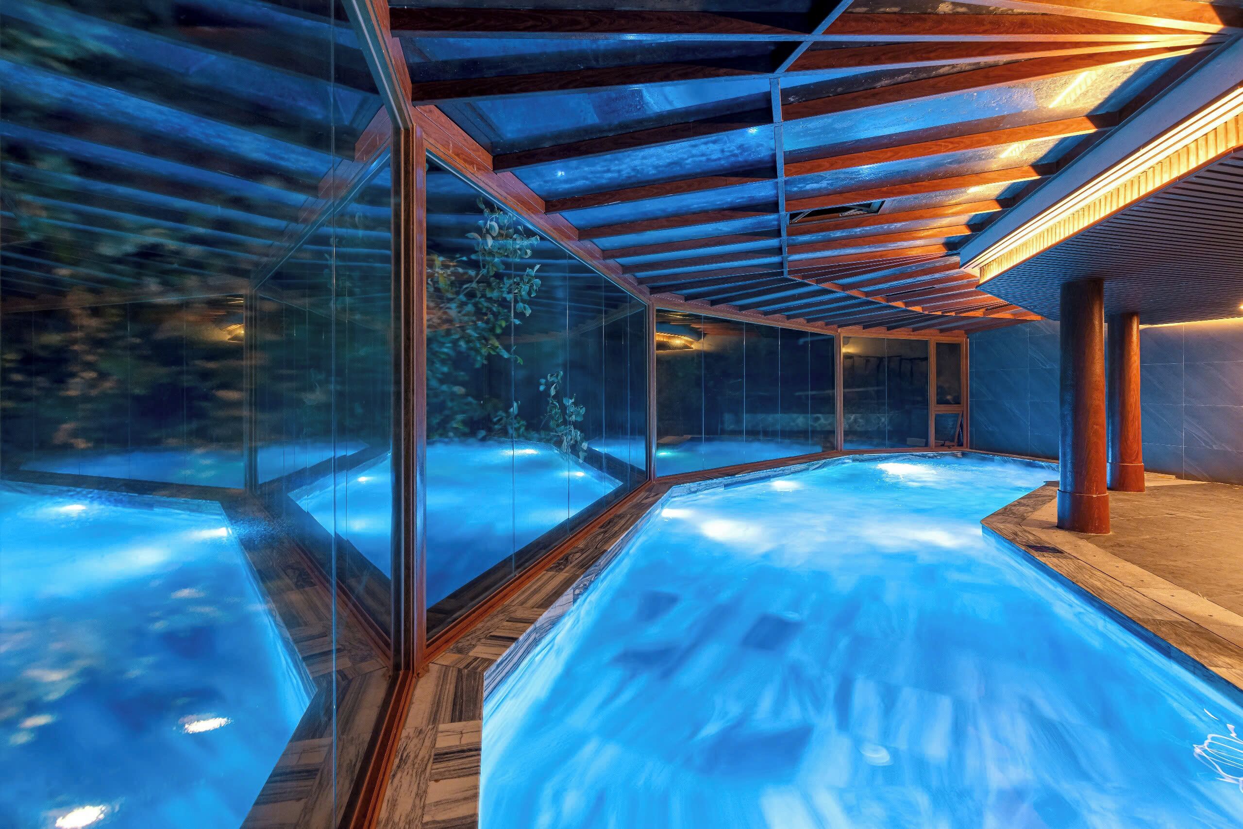 A modern spa with glass walls, wooden flooring, and a heated pool.