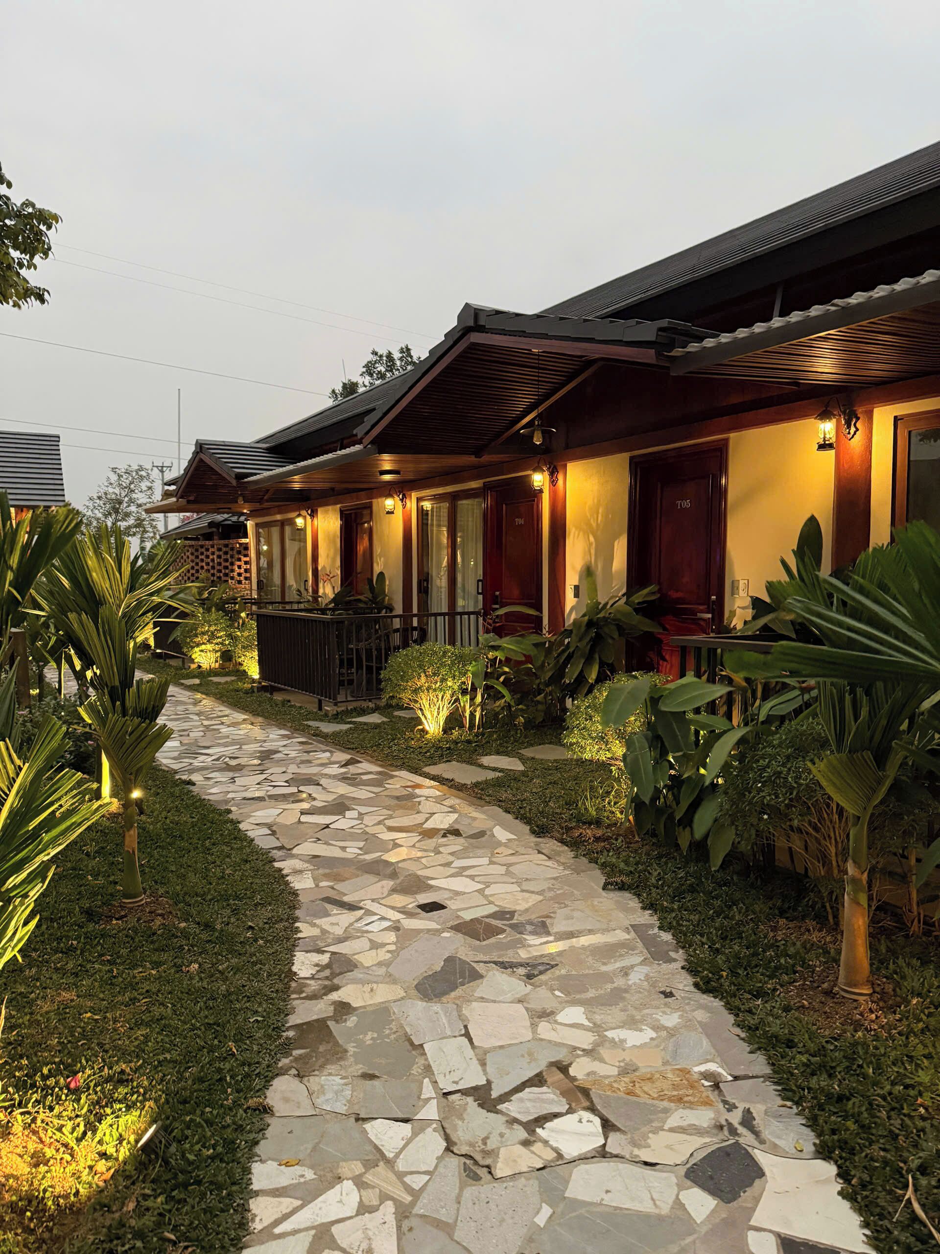 A hotel with a stone pathway leading to a series of rooms with wooden facades and warm lighting.