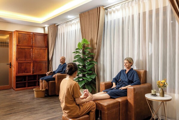 A room with a wooden cabinet, a large plant, and two people seated on leather chairs.