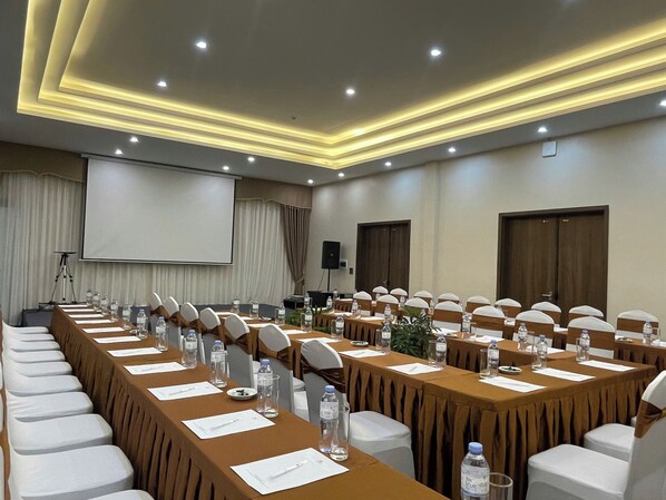 A conference room with long tables, chairs, and a projector screen.