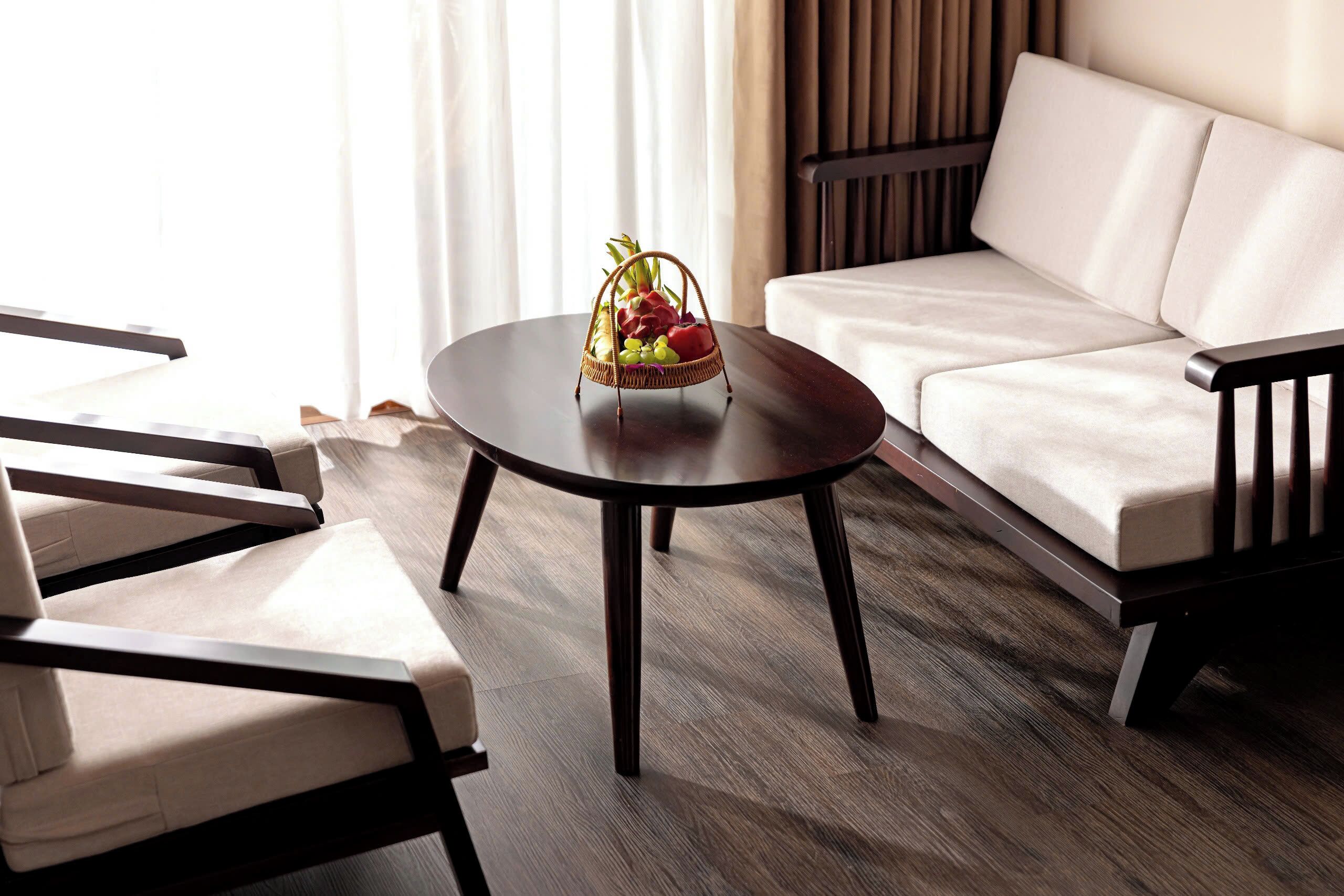 A modern living room with a round wooden coffee table, a beige sofa, and two armchairs.