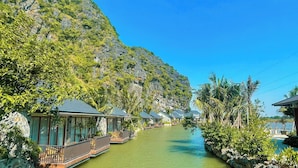 A canal with floating houses, surrounded by lush greenery and rocky cliffs. - Athena Premier Resort Ninh Bình (Nam Hoa Lu)