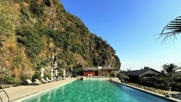 A clear swimming pool with lounge chairs and a building in the background. - Athena Premier Resort Ninh Bình (Nam Hoa Lu)