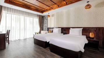 Habitación de hotel con dos camas, techo de madera, un ventanal grande con cortinas y una mesita con una silla.