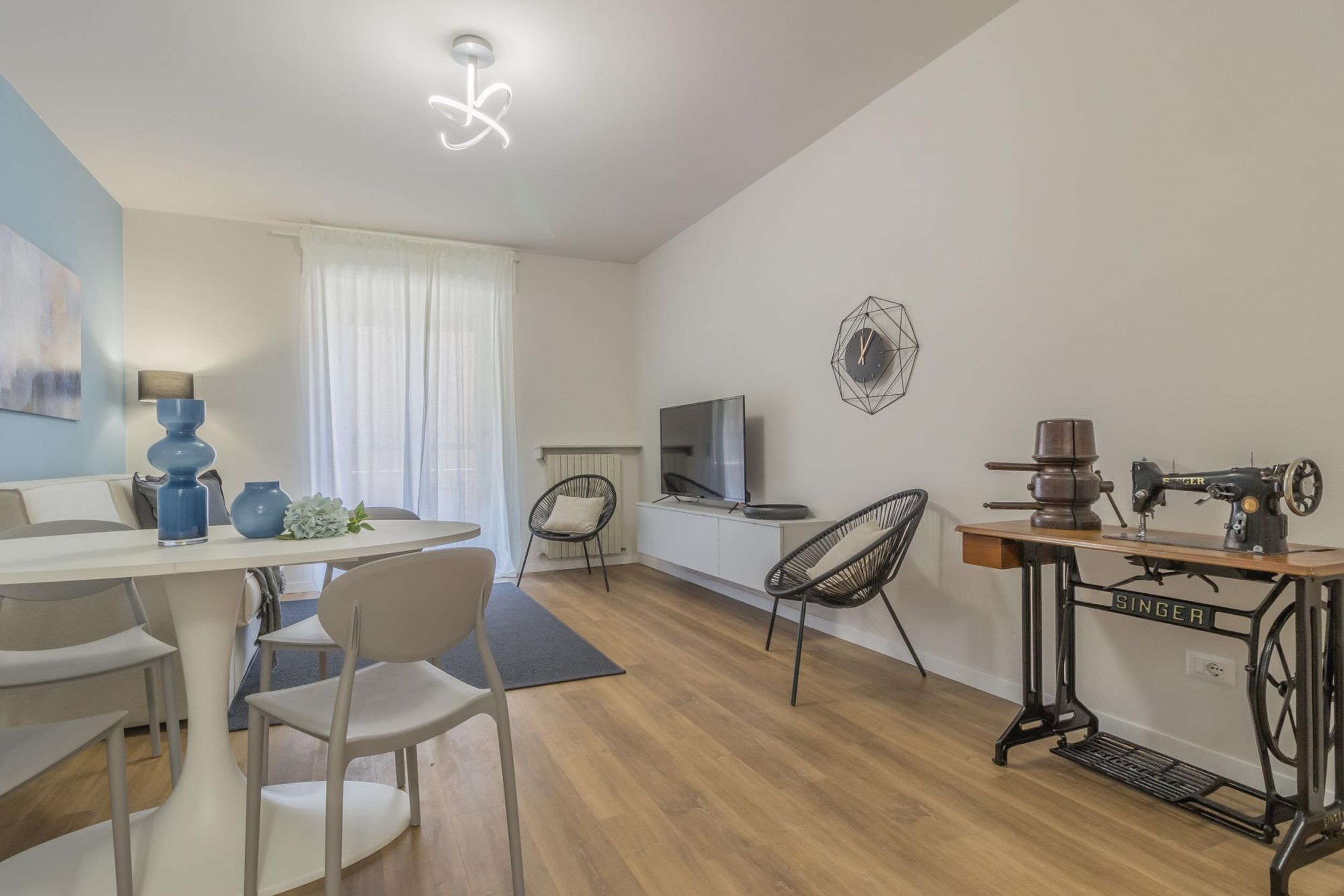 A modern living room with a dining area, a sewing machine, and a television.
