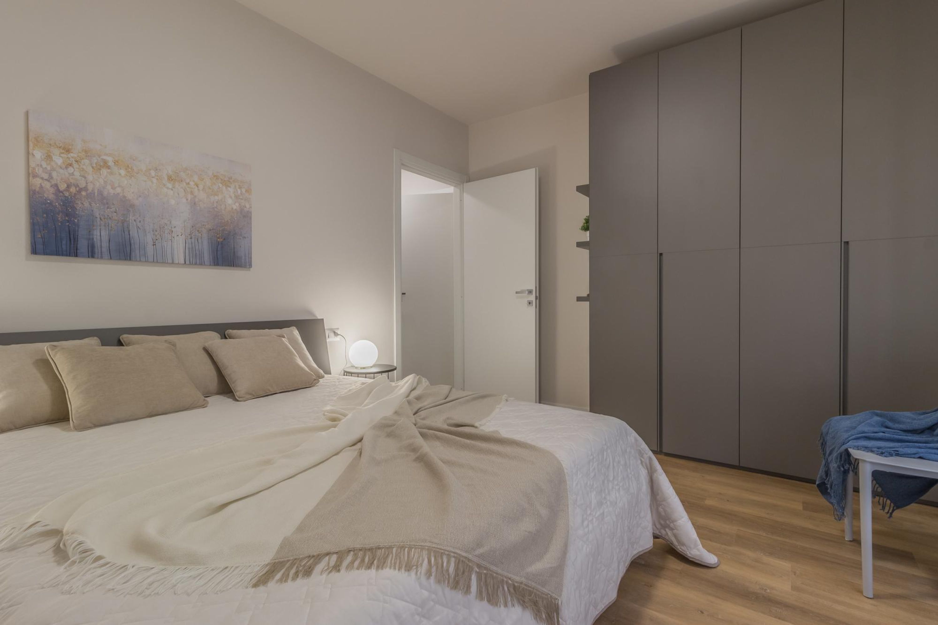 A bedroom with a bed, a bedside table with a lamp, a wardrobe, and a painting on the wall.