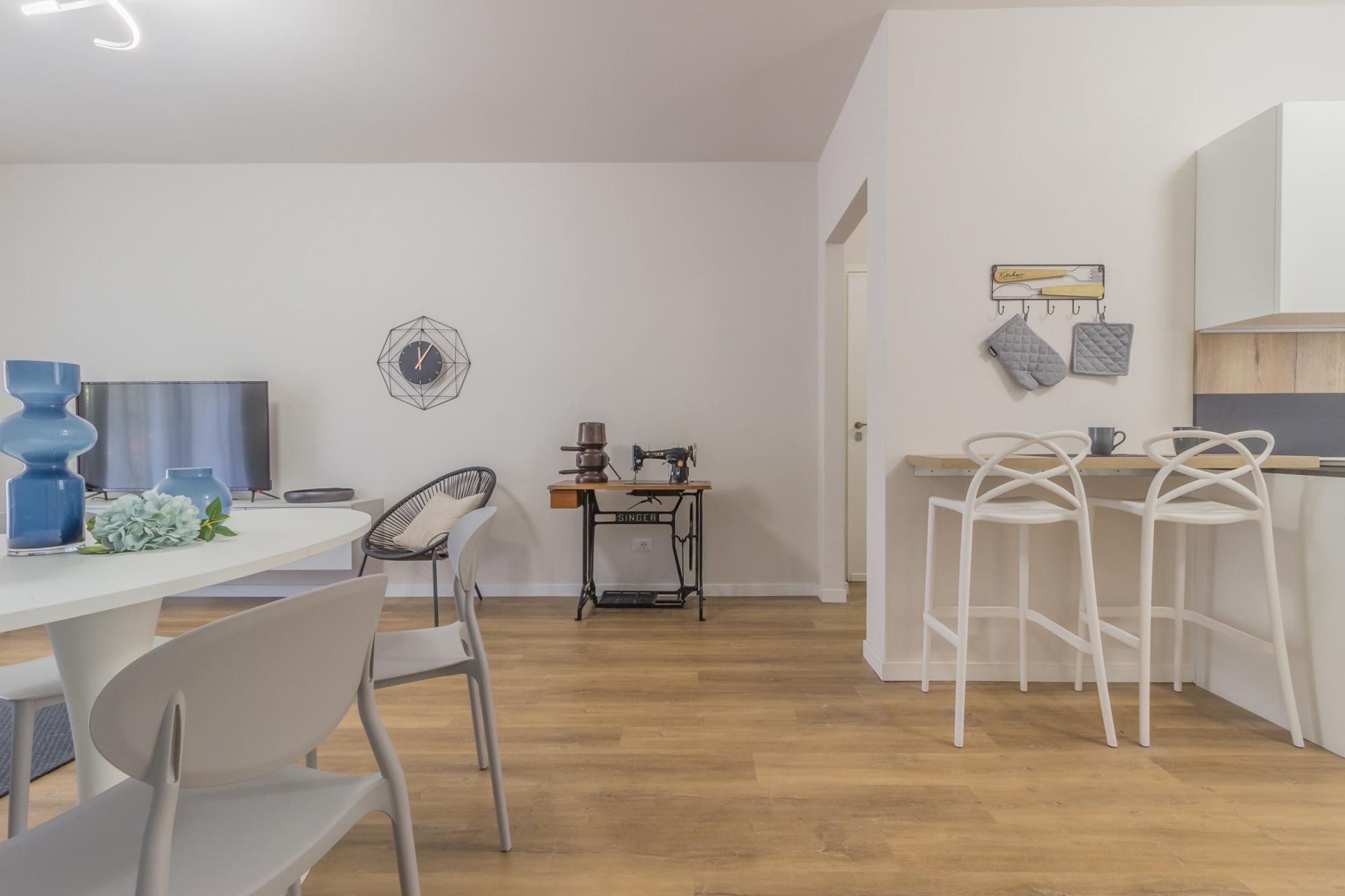 A modern kitchen with white bar stools, a sewing machine, and a wall-mounted rack with kitchen utensils.