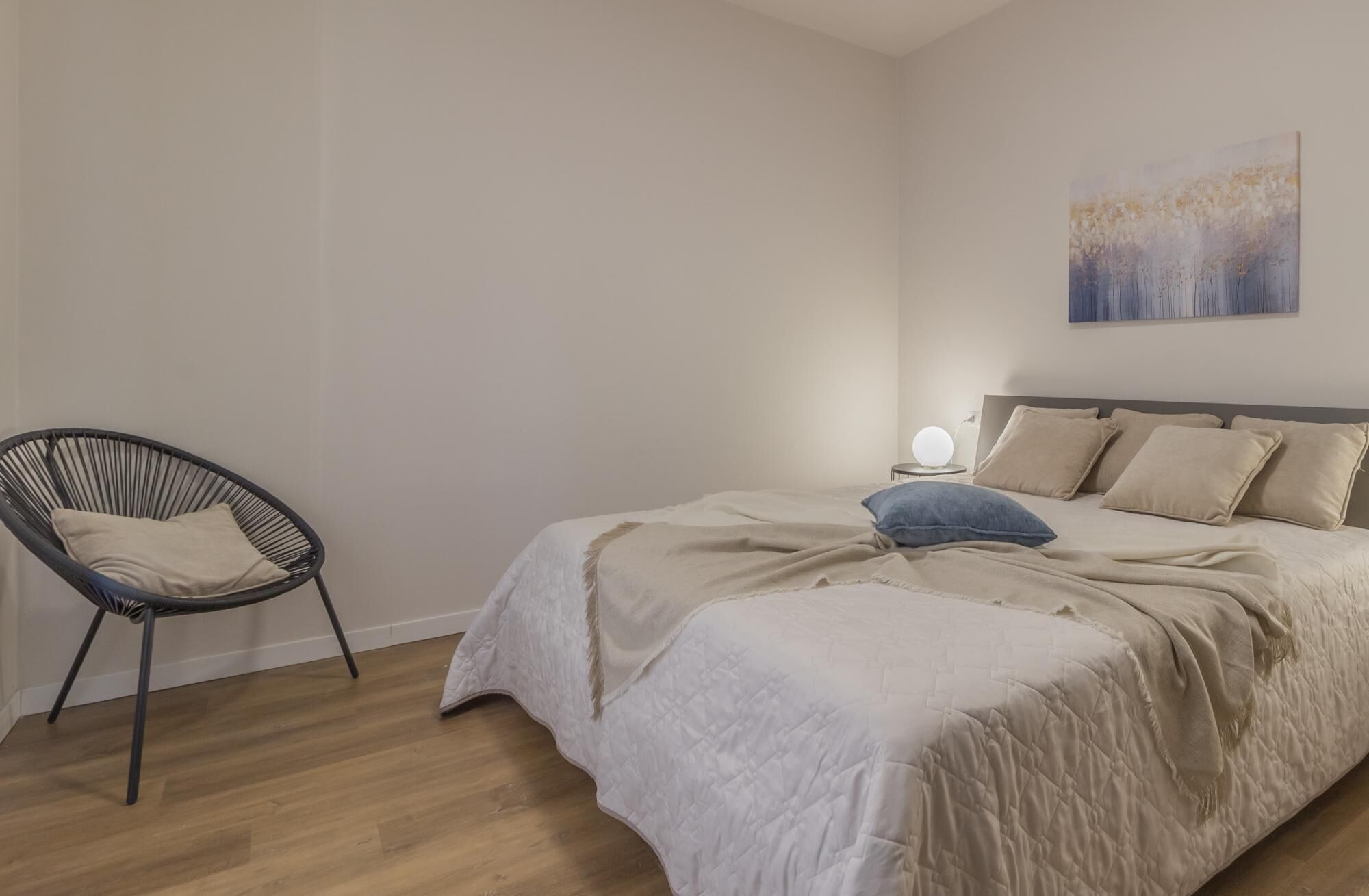 Un dormitorio con una cama, una silla y un cuadro en la pared.