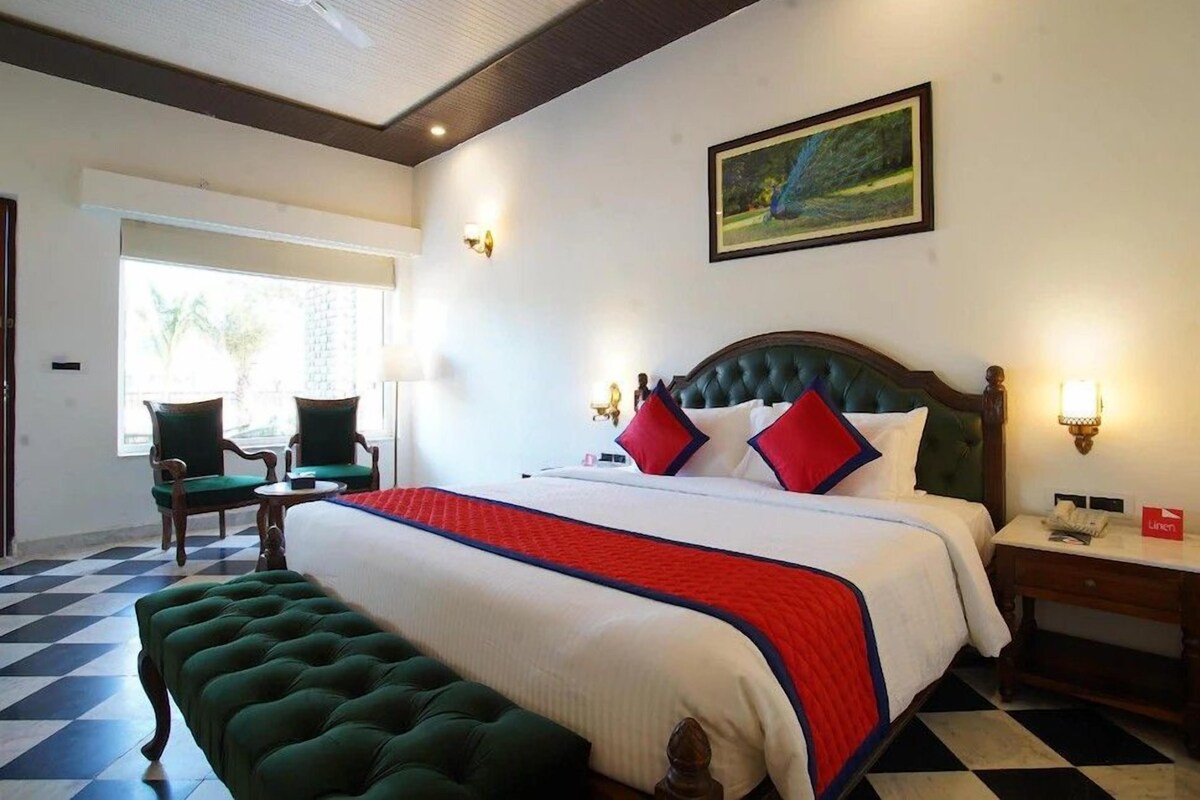 Une chambre d’hôtel avec un grand lit, un banc recouvert d’un tissu vert, un bureau et une chaise.