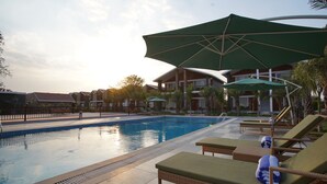A swimming pool with lounge chairs and umbrellas, surrounded by buildings and palm trees. - Spree Resort Sariska (Thanagazi)