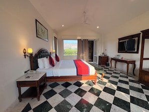 Una habitación de hotel con piso a cuadros, una cama con colcha roja y blanca, un escritorio con teléfono y un televisor en la pared.