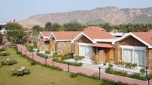 A row of brick houses with red roofs, a paved walkway, and a mountain backdrop. - Spree Resort Sariska (Thanagazi)