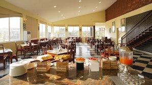 A spacious dining area with multiple tables and chairs, a buffet setup with various food items, and a large window providing natural light. - Spree Resort Sariska (Thanagazi)