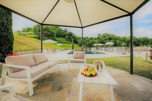 A covered outdoor seating area with a pool in the background.