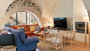 A cozy living room with a stone arch, a blue sofa, a wooden coffee table, wicker chairs, a television, and a fireplace. - Garriguella- Roses – Pool Costa Brava House (Garriguella)