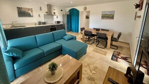 En moderne opholdsstue med en hjørnesofa, et spisebord med stole, et køkken og et mindre spisebord med stole.
