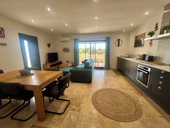 A modern living space with a dining area, sofa, kitchen, and a view to the outside.