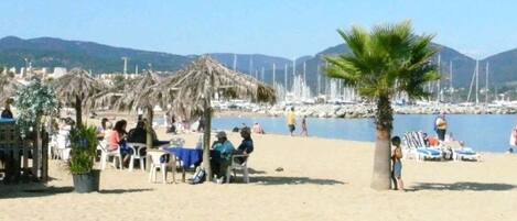A beach with thatched umbrellas, palm trees, and people relaxing.