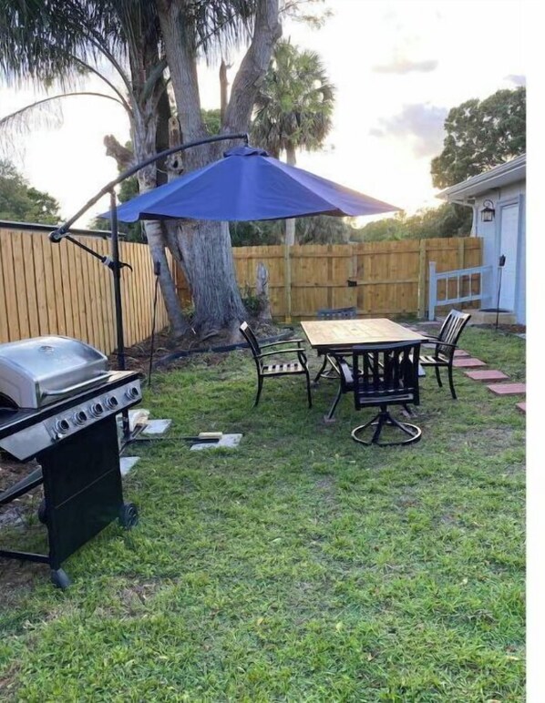 A backyard with a barbecue grill, a table with chairs, and a blue umbrella.