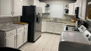 A kitchen with white cabinets, a black refrigerator, a microwave, and a washing machine.
