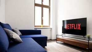 A modern living room with a blue sofa, a glass coffee table, and a TV displaying the Netflix logo.